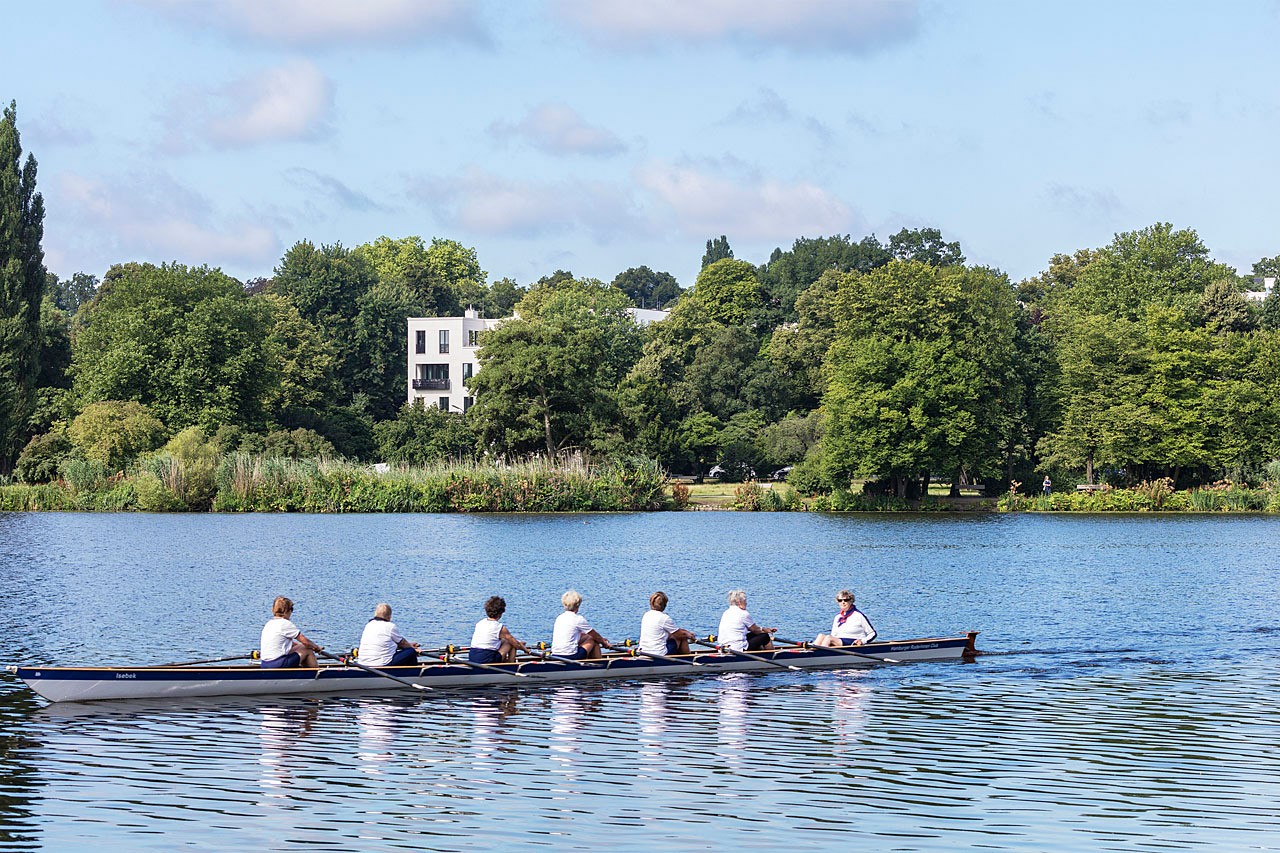Rowing crew on the Outer Alster, with a white Alster villa among the trees on the bank behind
