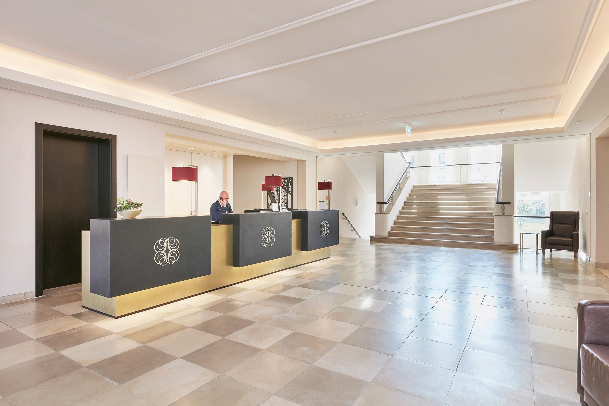 Concierge reception in the Sophienpalais with a dark desk, light stone floor and a staircase in the background