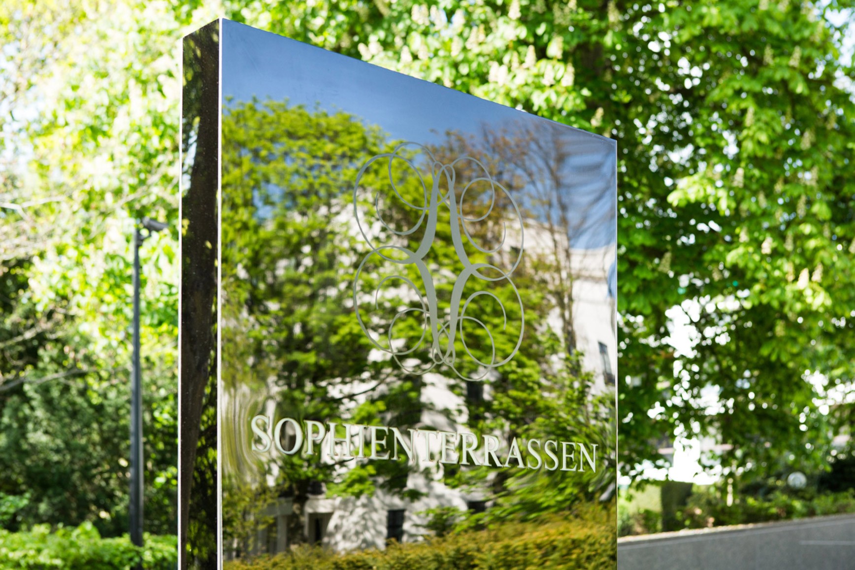 Mirrored sign stele with the Sophienterrassen logo and lettering among green trees
