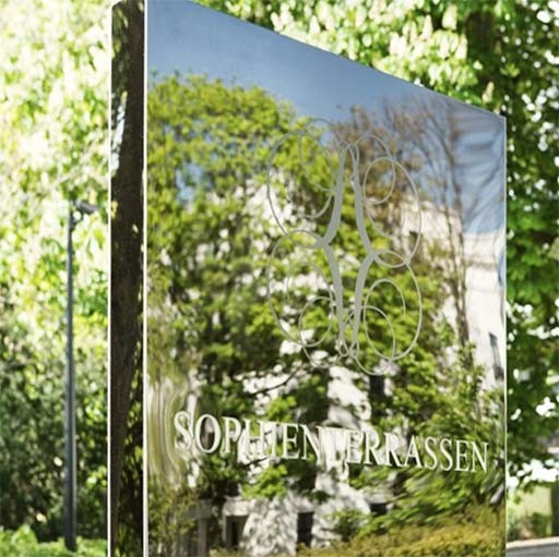 Spiegelnde Stele mit Sophienterrassen-Logo und Schriftzug, auf der sich die umliegenden Bäume spiegeln