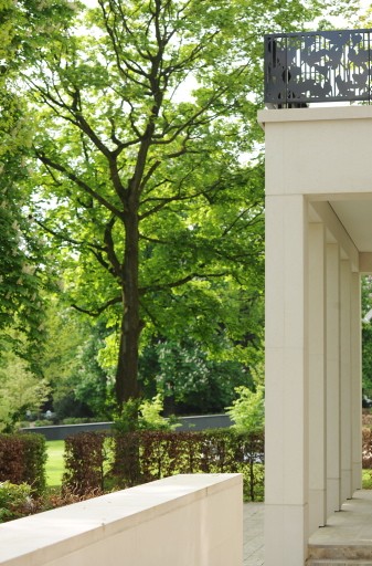 Seitlicher Blick an einer Pfeilerloggia der Alstervillen vorbei auf hohe Laubbäume und parkartiges Grün