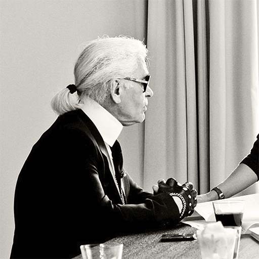 Schwarz-Weiß-Aufnahme von Karl Lagerfeld im Profil, mit Sonnenbrille an einem Tisch sitzend