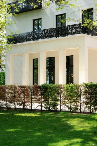 Weiße Villa der Alstervillen mit Pfeilerloggia im Erdgeschoss, ornamentalem Balkongeländer und Hecke vor dem Rasen
