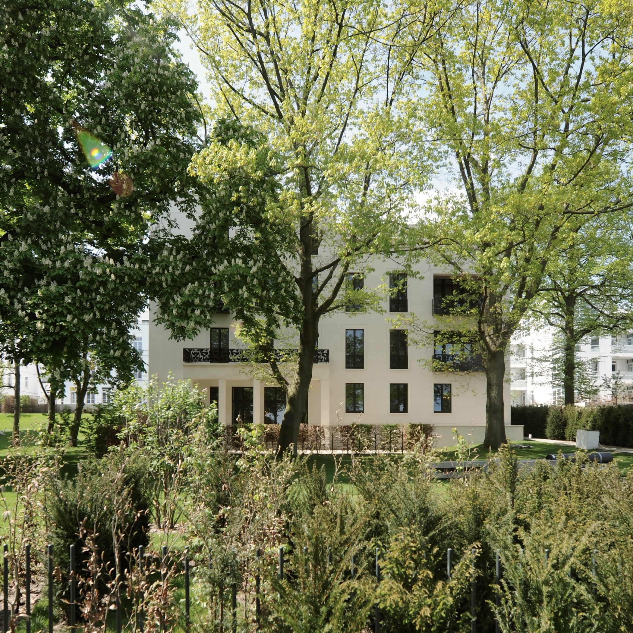 Weiße Villa der Alstervillen hinter hohen Laubbäumen und dichter, naturnaher Gartenbepflanzung