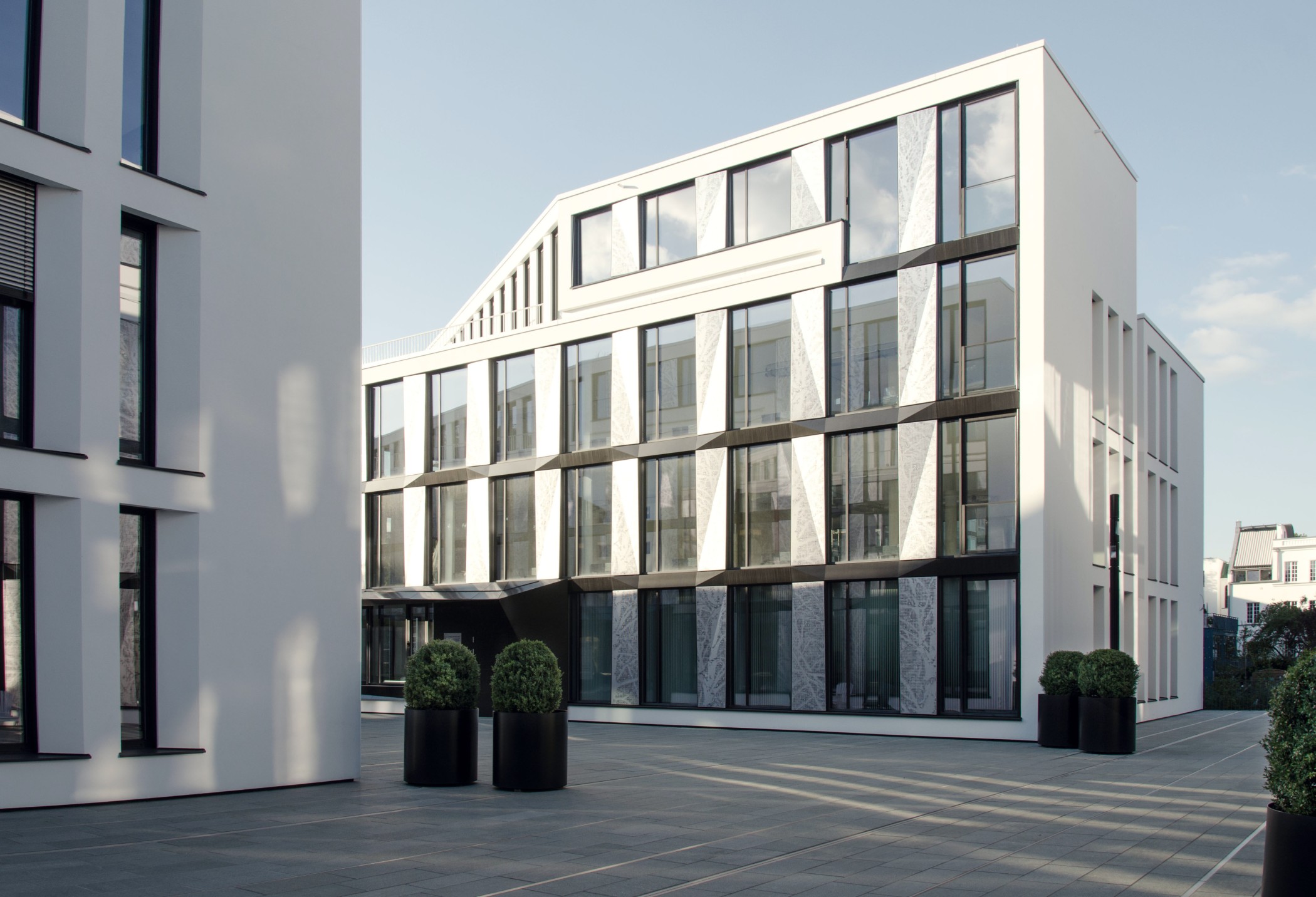 Office-Gebäude von Carsten Roth mit schräger Dachkante, großen Glasflächen und Pflanzkübeln am Quartiersplatz
