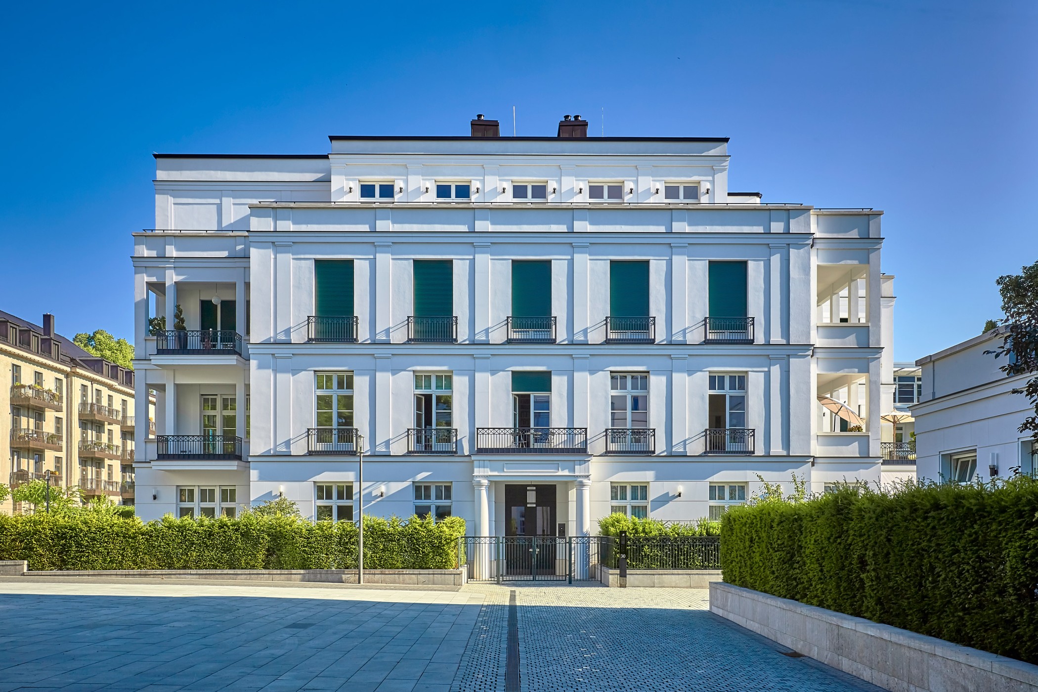 Front view of a neoclassical white villa of the Alster villas with green shutters and a paved forecourt