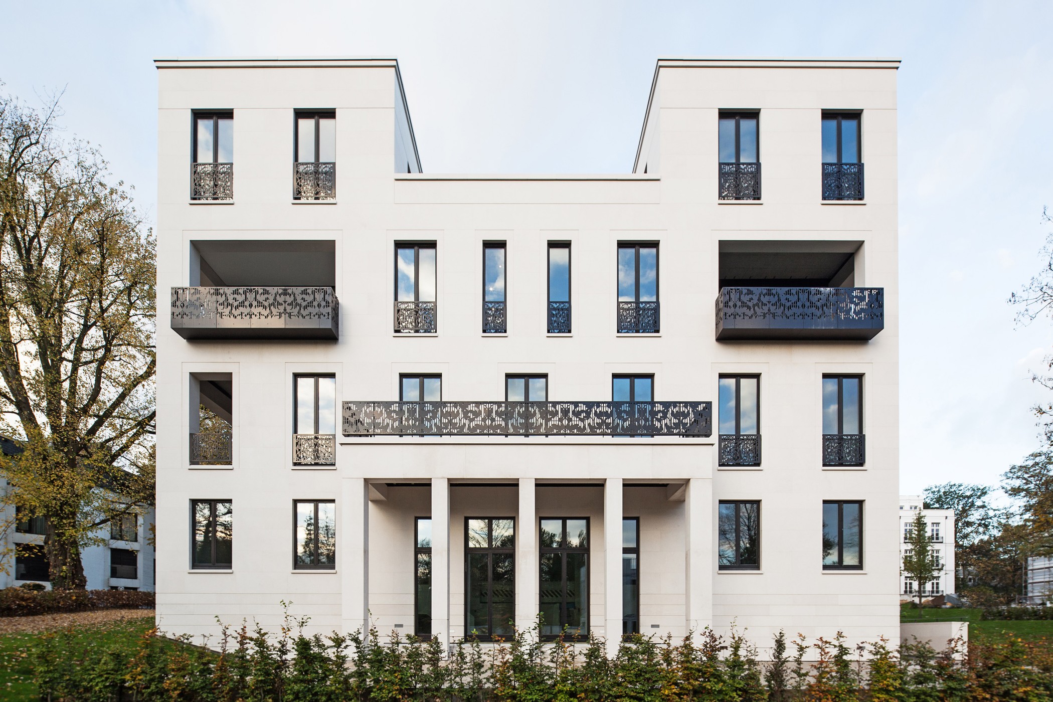 Frontansicht der Sophienterrassen in Hamburg, moderne Luxuswohnung im Stil der Alstervillen mit heller Natursteinfassade, hohen Fenstern und kunstvollen schwarzen Balkongeländern, eingebettet in eine ruhige Gartenanlage