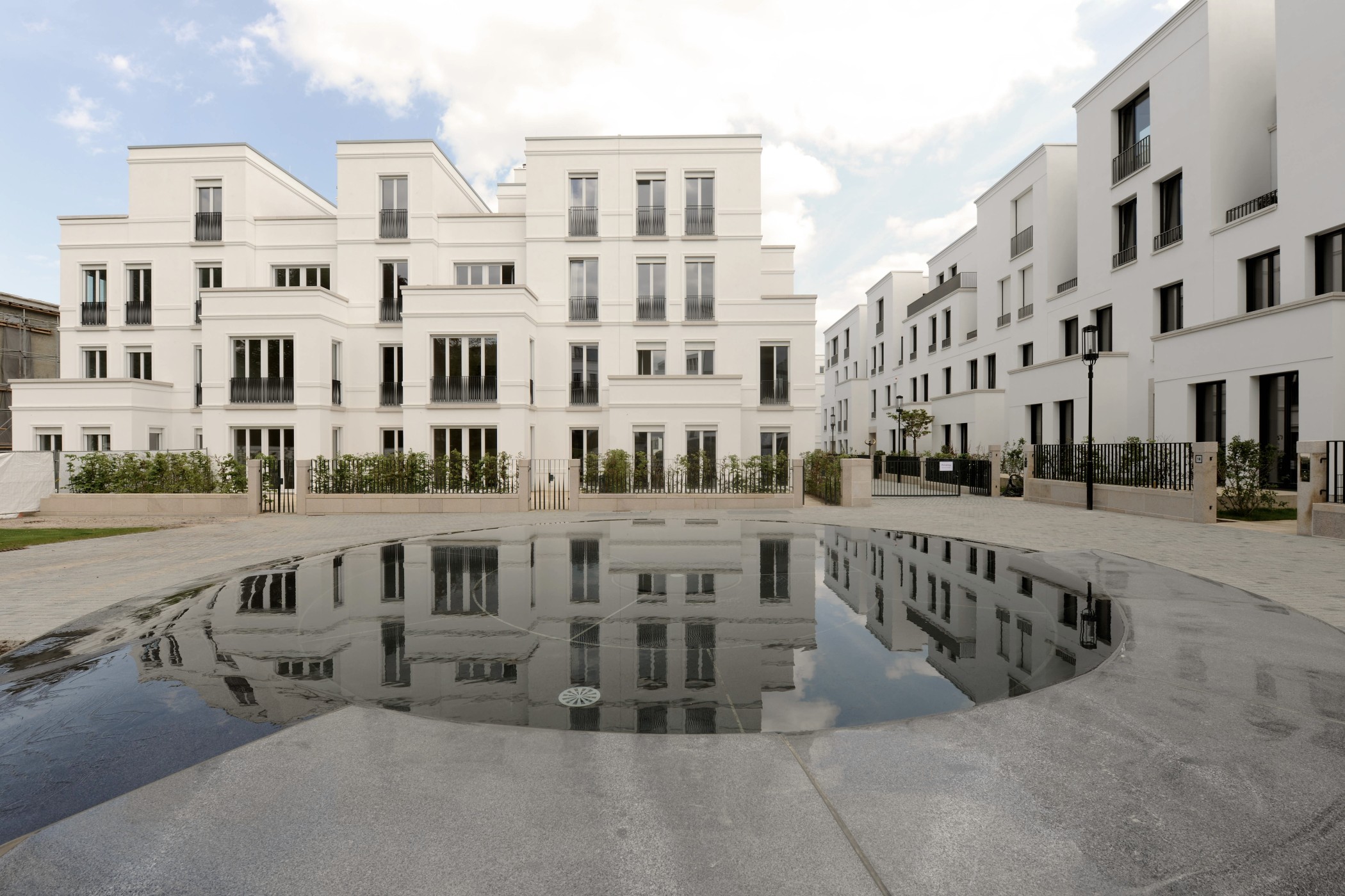 Ansicht der eleganten Townhouses der Sophienterrassen mit weißer klassizistischer Architektur, großen Fensterformaten und Spiegelung der Gebäude im zentralen Wasserbecken einer Luxuswohnung