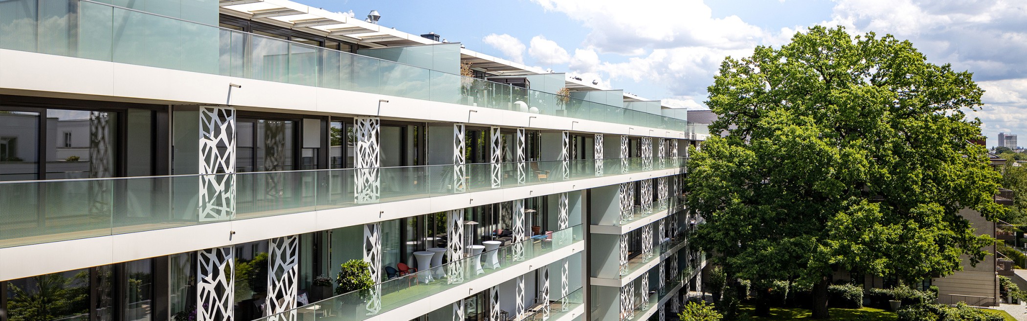 Moderne Fassadenansicht der Sophienterrassen in Hamburg mit großzügigen Glasbalkonen, dekorativen Metallpanelen und Blick auf die alte Eiche – hochwertige Architektur einer exklusiven Luxusimmobilie
