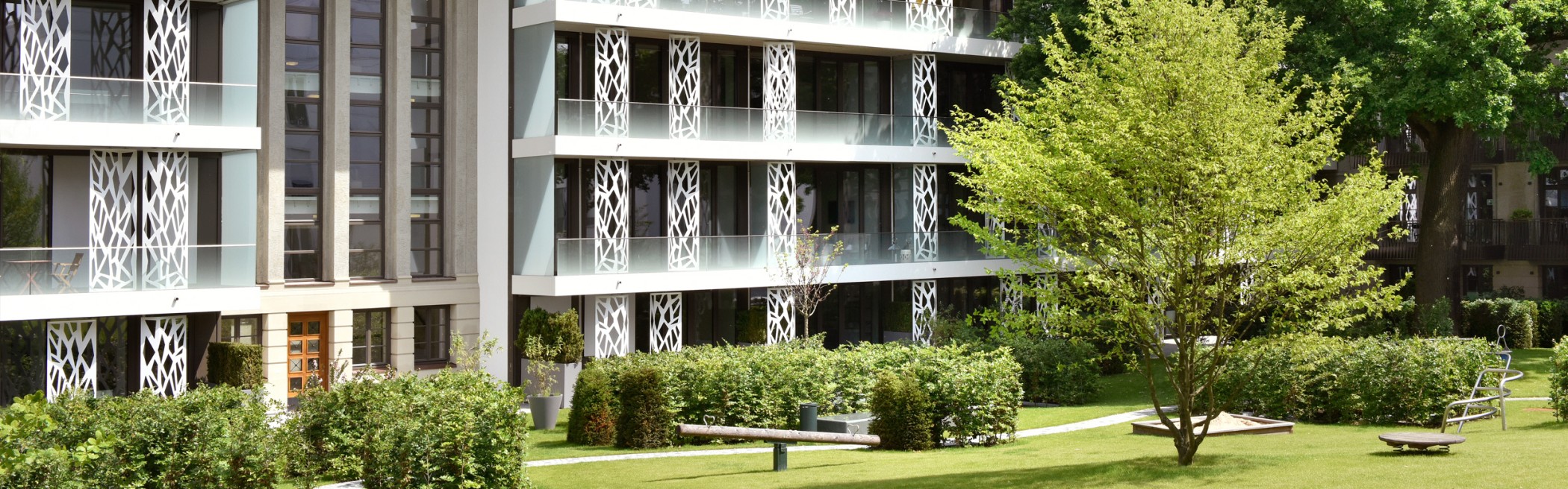Moderne Fassadenansicht der Sophienterrassen in Hamburg mit großzügigen Glasbalkonen, dekorativen Metallpanelen und Blick auf die alte Eiche – hochwertige Architektur einer exklusiven Luxusimmobilie