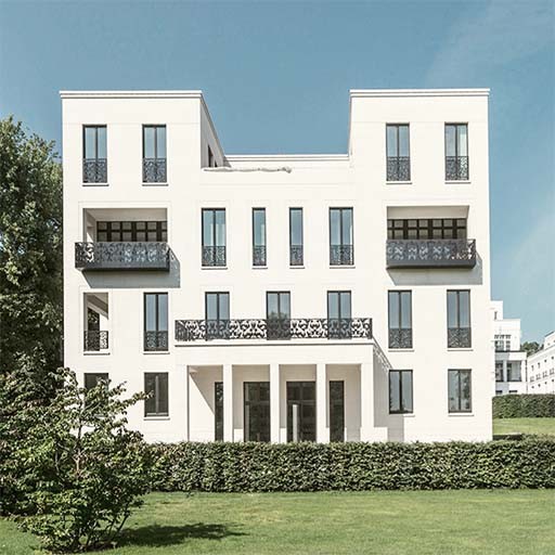 Gartenfassade einer weißen Alstervilla mit schwarzen Ziergittern an den Balkonen, Hecke und Rasen